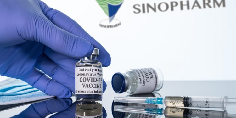 Morgantown, WV - 16 December 2020: Small bottle of coronavirus vaccine with syringe with background of the Chinese company Sinopharm logo