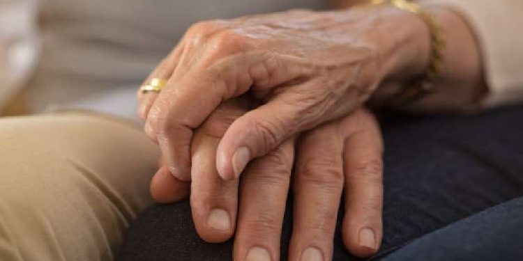 Closeup of elderly couple holding hands while sitting on couch. Husband and wife holding hands and comforting each other. Love and care concept.
